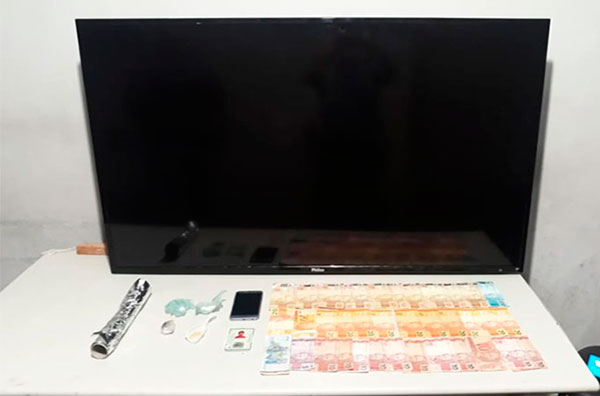 Divulgação PM - Foram apreendidas porções de drogas, um televisor de 55” e mais de R$ 1 mil em dinheiro Divulgação PM - Foram apreendidas porções de drogas, um televisor de 55” e mais de R$ 1 mil em dinheiro